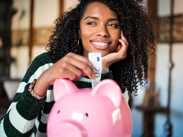 young woman putting monmey in a pink piggy bank